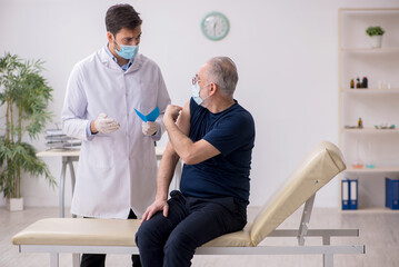 Fototapeta premium Old male patient visiting young male doctor in vaccination conce
