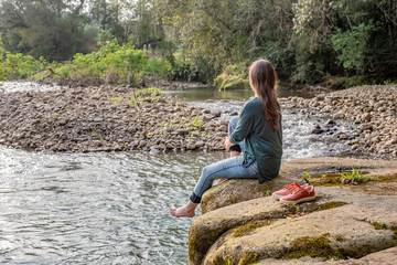 Woman sitting on a rock holding her leg. Woman relaxing in nature.