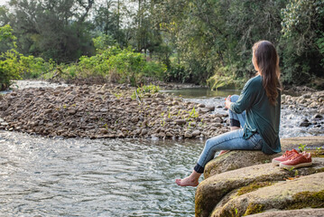 Woman sitting on a rock holding her leg. Woman relaxing in nature