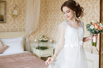 Fototapeta premium Pretty young Bride.Brown-haired woman with classic wedding hair-style. Boudoir morning of the bride. Taking a little candle in her hands