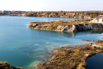 Autumn landscape with different colors of nature from the hills of a cretaceous quarry with a clean, transparent turquoise lake and a plant in the distance