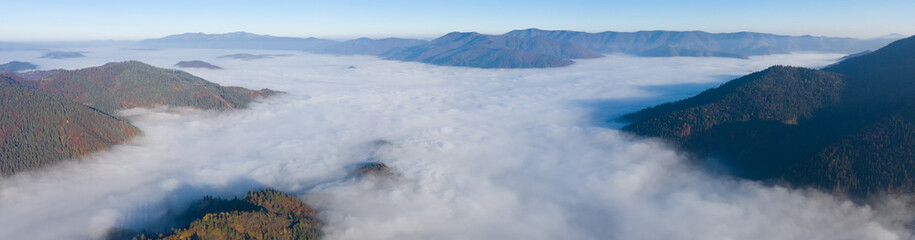 Autumn mountain landscape panorama. Peaks above the fog. Drone view.