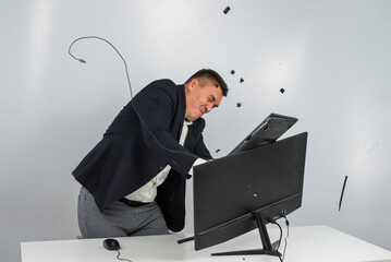 Caucasian man in a suit gets angry and smashes the keyboard on the monitor. An office worker in a rage breaks the computer. - obrazy, fototapety, plakaty