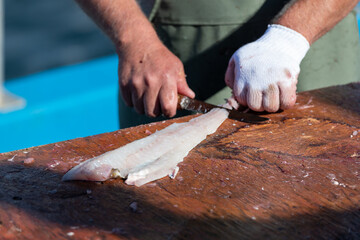 A closeup of a chef fillets and cleans codfish on a wood cutting board on a wharf with a knife. The fresh white Atlantic codfish is cut and prepared into loins, steaks, and filets for restaurants.