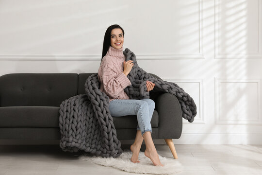 Young Woman With Chunky Knit Blanket On Sofa At Home