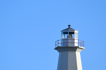 The watch room of a vintage eight-sided lighthouse. The lantern room has a large green bulb. The concrete building is white with a white rail around the gallery deck. The background is a blue sky.