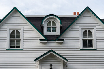 A white wood clapboard siding vintage house with multiple windows. The center window has a curved...