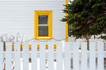 The exterior of a white clapboard wooden home with two bright yellow trim double hung windows and a...