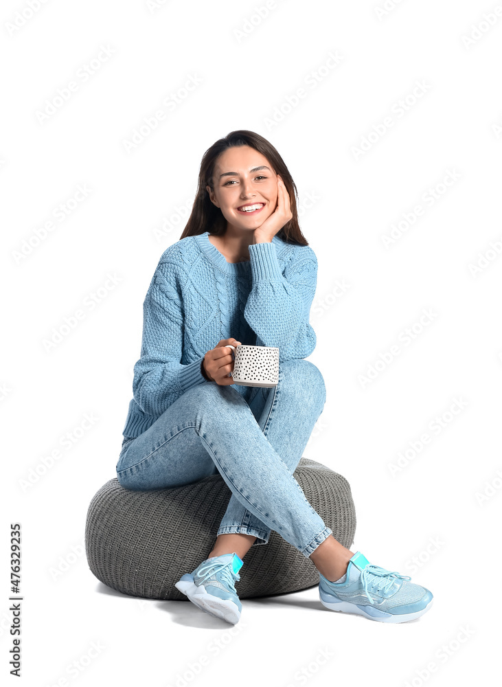 Sticker Beautiful woman with cup of coffee sitting on pouf against white background