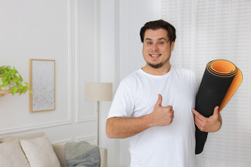 Overweight man with yoga mat at home, space for text