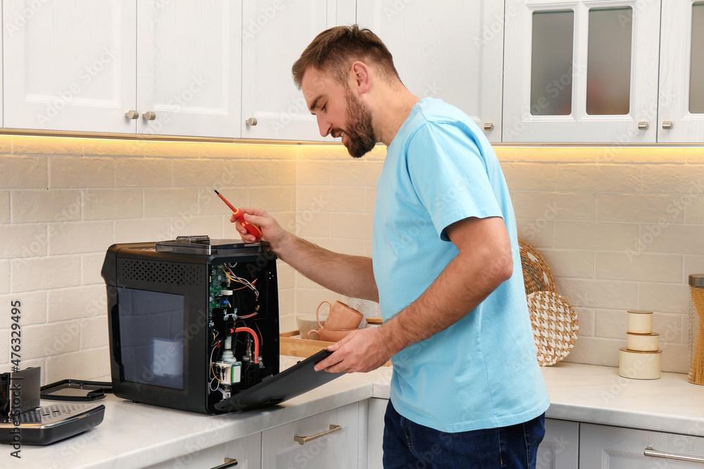 Sticker man with screwdriver fixing coffee machine at table in kitchen