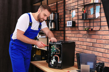 Repairman with screwdriver fixing coffee machine at table indoors