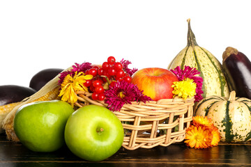 Basket with different healthy food on dark wooden table against white background. Harvest festival