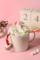 Cup of tasty cacao with candy cane and marshmallows on pink background