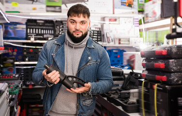Confident glad cheerful man buys electric stapler in tools store