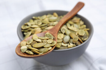 Bowl with pumpkin seeds and wooden spoon on tablecloth, closeup