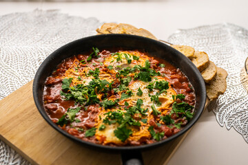 Shakshouka with tomatoes, peppers eggs, on a hot pan with crout croutons sprinkled with chives