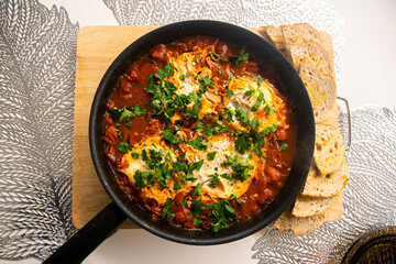 Shakshouka with tomatoes, peppers eggs, on a hot pan with crout croutons sprinkled with chives