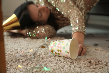 Drunk young woman with empty cup sleeping after Christmas party at home