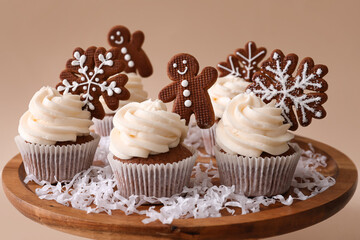Wooden stand of tasty Christmas cupcakes with gingerbread cookies on beige background