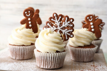 Tasty Christmas cupcakes with gingerbread cookies on table