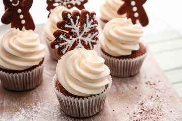 Wooden board of tasty Christmas cupcakes with gingerbread cookies on table