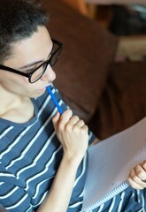 close up of a young man with glasses sitting on the sofa thinking what to write in his notebook. study concept. writing concept. 