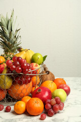 Metal basket with different fresh fruits on white marble table