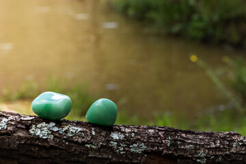 Two green quartz crystals supported by a tree branch with a beautiful blurred lake in the background illuminated by sunlight
