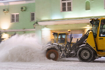 Snow plow truck cleaning street at night in snowy storm. Snow removal vehicle on city road after...
