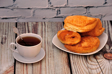 A cup of black tea on the table and a plate with an assortment of fresh puff pastries.