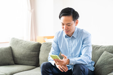 部屋でスマホを見る男性