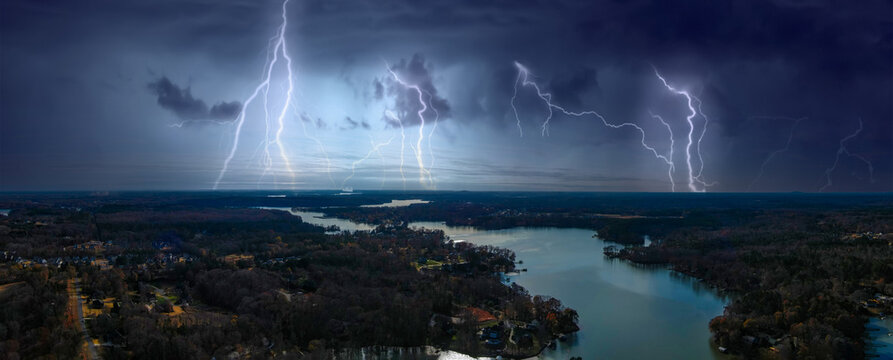 a stunning aerial panoramic shot of the silky green Catawba River surrounded by vast miles of green and autumn colored trees with powerful clouds and lightning in the sky in Charlotte North Carolina