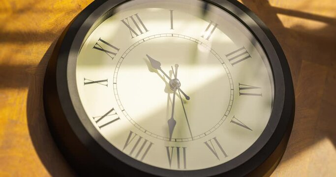 Time lapse of a antiquated wall clock on wooden background. Shadows and reflections from the sun streak across the clock. Traditional wall clock with running time pointer on white clock face. 