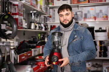 Adult glad positive smiling male is standing with new mixer for his home in the store