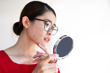 Portrait of worried Asian woman with bad emotional while looking acne and scar occur on her face by mini mirror. Conceptual shot of Acne and Problem Skin on female face.