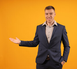 smiling man in business suit with empty open palm on yellow background, copy space