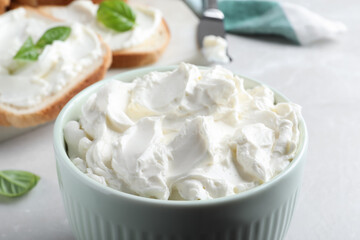 Bowl of tasty cream cheese on grey table, closeup