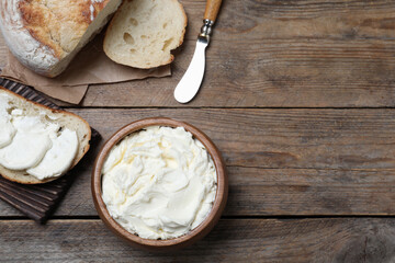 Fresh bread with delicious cream cheese on wooden table, flat lay. Space for text