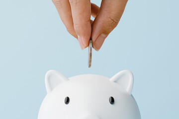 Save money and investment concept. Hand with coin dropping in piggy bank on light blue background