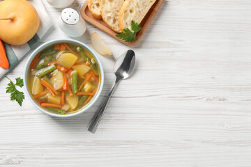 Bowl of tasty turnip soup with bread and spoon on white wooden table, flat lay. Space for text