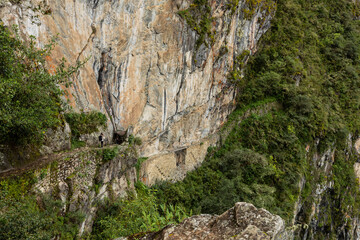 Obraz premium A female tourist walks on the narrow path towards a tiny door in the mountain, Machu Picchu, Peru