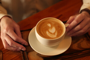 Woman with cup of aromatic coffee at wooden table, closeup