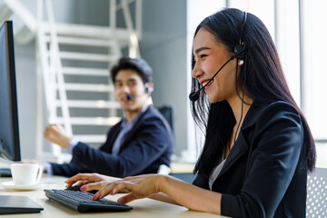 Asian happy female telemarketer receptionist operator service support employee staff in formal suit wears headset smiling typing keyboard while having conversation discussing helping customers online