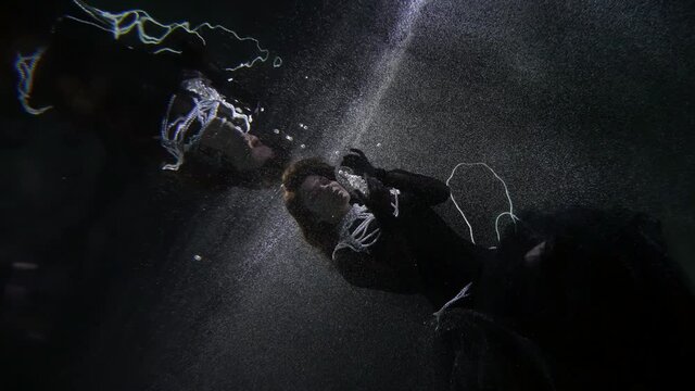 underwater magic, mysterious woman in black dress is playing with pearls, swimming in deepness