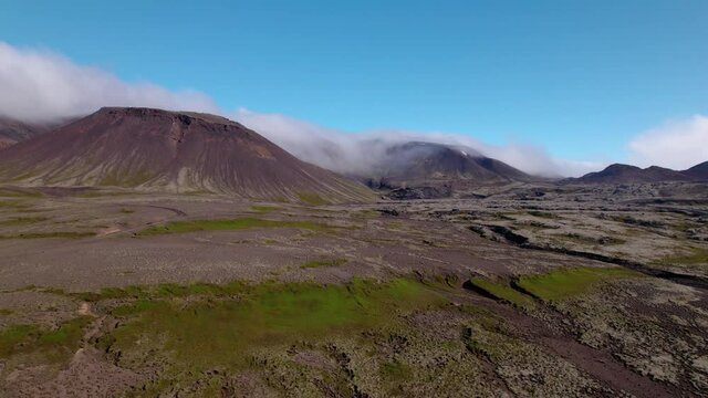 Rising aerial shot over dramatic Iceland landscape of dormant volcano and lava field. Fog and mist surrounds the mountains.