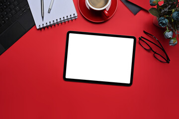 Top view digital tablet, coffee cup, glasses and notebook on red background.