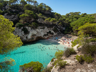 Cala Macarelleta en Menorca, Islas Baleares, España, con su agua de color turquesa y su arena dorada en un día soleado. Gente bañandose y tomando el sol.