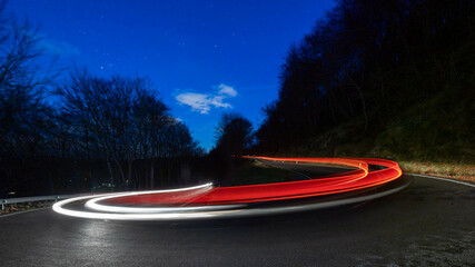Trazas provocadas por las luces de un vehículo al coger una curva en una carretera de montaña en...