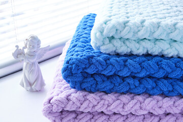Warm, delicate and plush handmade baby blankets in three colors of blue, lilac and mint on background of window.